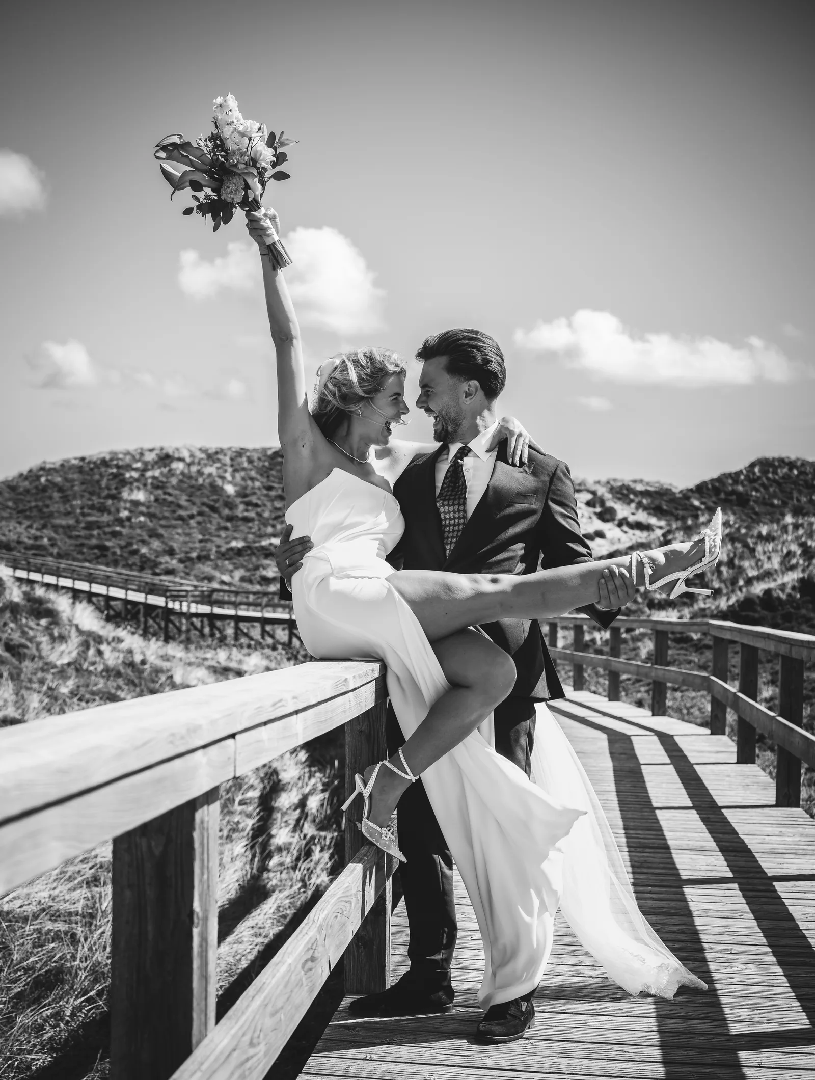 Hochzeitsfotograf Sylt — Braut jubelt mit Brautstrauß auf dem Holzsteg in den Dünen