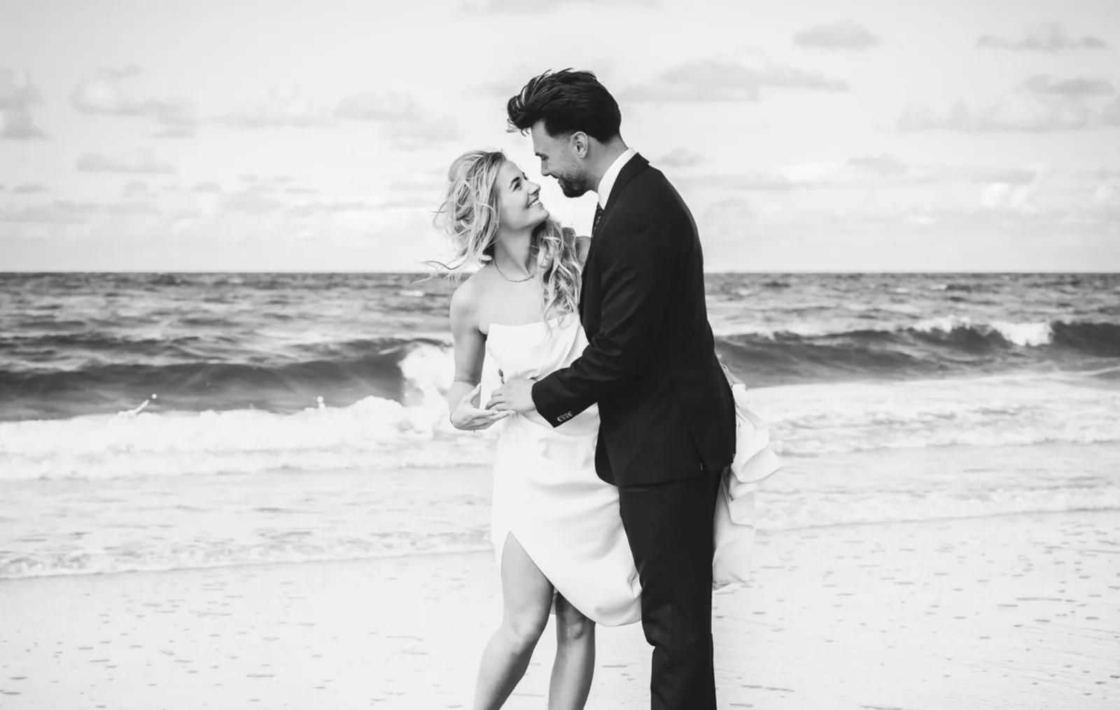 Hochzeitsfotograf Sylt — Brautpaar lacht sich am Nordseestrand an, im Hintergrund die Brandung